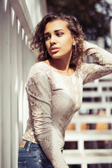 Close up portrait of a beautiful young woman with curly hair smiling outdoors near the stairs