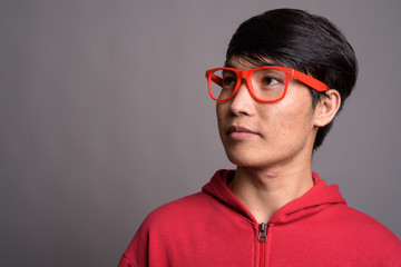 Young Asian man wearing red jacket with eyeglasses against gray 