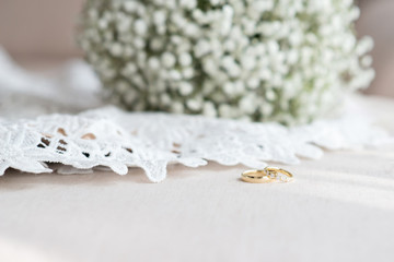 Wedding rings and a bridal bouquet over a white lace wedding dress - selective focus, copy space