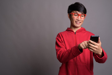 Young Asian man wearing red jacket with eyeglasses against gray 
