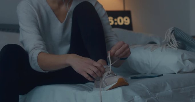 Attractive sporty young Caucasian woman getting ready for exercising early in the morning, tying her sports shoe. 4K UHD