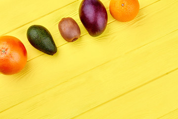 Row of tropical fruits and copy space. Assortment of exotic fruits including grapefruit, kiwi, mango and orange on yellow wooden background.