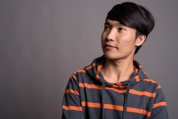 Young Asian man wearing striped hoodie against gray background