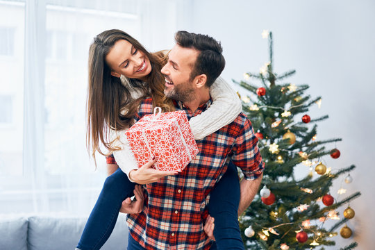 Cheerful couple holding present and goofing around in christmas decorated living room