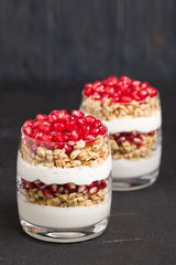 Pomegranate parfait - sweet organic layered dessert with granola flakes, yogurt and fruit seeds on black background.
