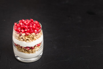 Pomegranate parfait - sweet organic layered dessert with granola flakes, yogurt and fruit seeds on black background.