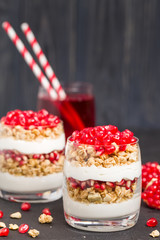 Pomegranate parfait - sweet organic layered dessert with granola flakes, yogurt and fruit seeds on black background.