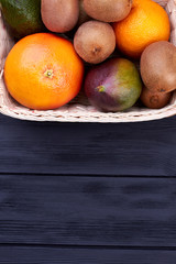 Variety of tropical fruits and copy space. Fresh colorful fruits in basket on dark wooden surface and text space, top view. Fruits summer harvest.