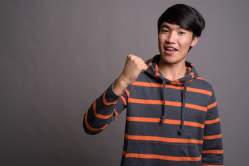Young Asian man wearing striped hoodie against gray background