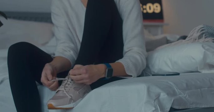 Attractive sporty young Caucasian woman getting ready for exercising early in the morning, tying her sports shoe. 4K UHD