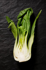 Half of fresh bok choy, pac choi, chinese cabbage on a black stone background, top view