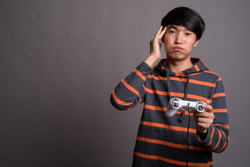 Young Asian man playing games against gray background