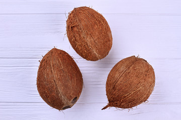 Three ripe coconuts, top view. Delicious tropical fruits on light wooden background. Healthy exotic...