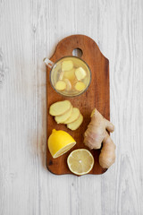 Mug of homemade ginger tea with lemon on wooden board over white wooden surface, top view. Flat lay, overhead, from above.