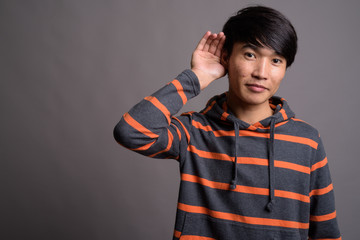 Young Asian man wearing striped hoodie against gray background