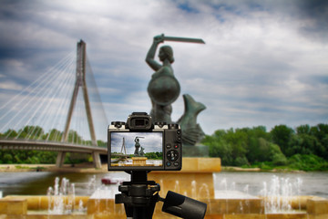 Camera and Monument of the Mermaid in Warsaw against the background of the Świętokrzyski Bridge and the Vistula River - obrazy, fototapety, plakaty