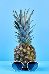 Pineapple and sunglasses on blue background. Whole hawaiian ananas and sunglasses. Summer holiday...