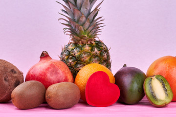 Composition from exotic fruits on pink background. Assortment of tropical fruits on wooden surface. Healthy food with love.