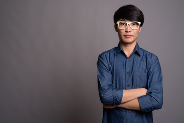 Young Asian man wearing eyeglasses looking smart against gray ba