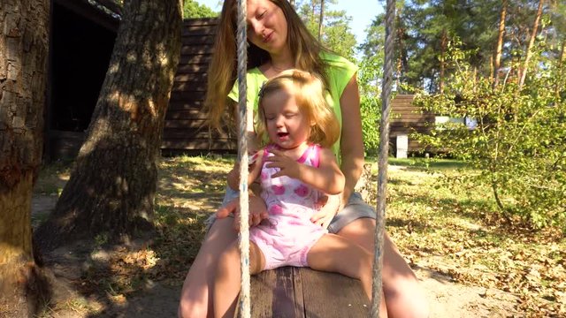 Mother and daughter on wooden flip-flap under tree