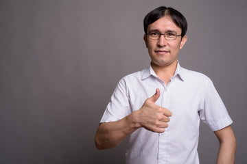 Young Asian nerd man wearing eyeglasses against gray background