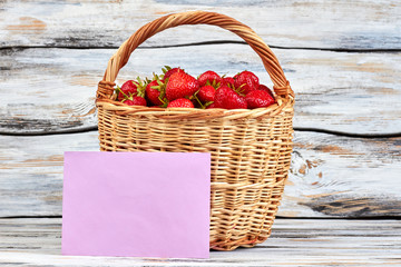 Basket of strawberries and blank paper card. Ripe organic strawberries in wicker basket on vintage...
