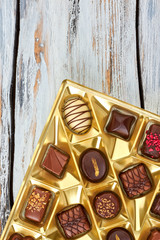 Set of delicious chocolate candies in box. Box filled with chocolate pralines on vintage wooden boards. Tasty sweet present.