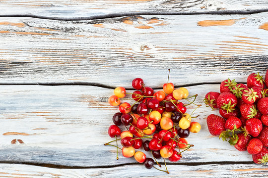 Heap of fresh cherries and strawberries. Ripe berries on wooden background and copy space. Healthy summer fruits.