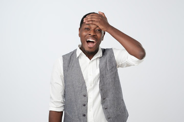 African man remembering funny momen laughing out loud from joy and happiness holding hands on head