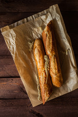Fresh baguetteon paper bag, on wooden table, close up