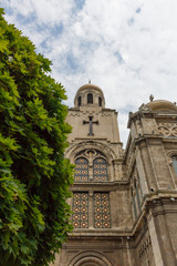 Fototapeta na wymiar Upward view of Dormition of the Mother of God Cathedral in Varna, Bulgaria, with tree, on the cloudy blue sky day