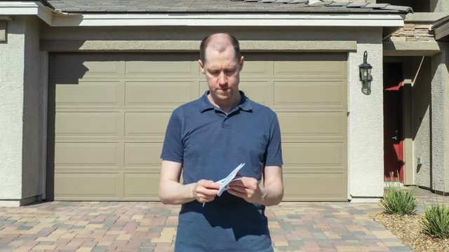 A home owner opens an Official Notification envelope to read the Final Notice letter within, showing a look of shock and dismay on his face; dolly zoom effect.