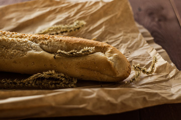 French baguettes with sesame seed on a paper bag lie on a wooden table.