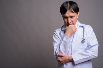 Young Asian man doctor against gray background