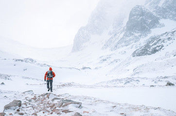 Climber walks alone in high mountains at windy snowy weather