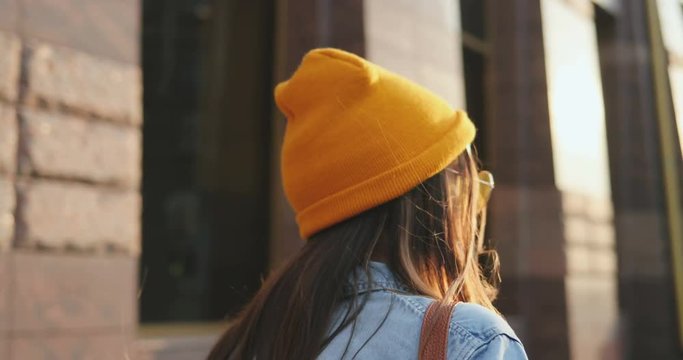 Back view on the Caucasian girl in hipster smile walking the city, then turning to the camera and smiling. Close up. Rear. Portrait. Outside.