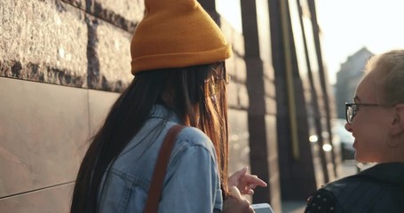 Rear of the Caucasian stylish girls best friends walking the street withe smartphones and talking cheerfully. Close up. back view, Outdoor.