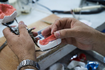 Dental technician using a knife with ceramic dental implants in his laboratory.  Dentist working with tooth dentures in his lab office 