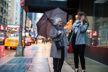 Two women talking under an umbrella on New York city sidewalk