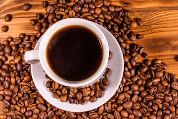 Cup of hot coffee and scattered coffee beans on wooden table. Top view