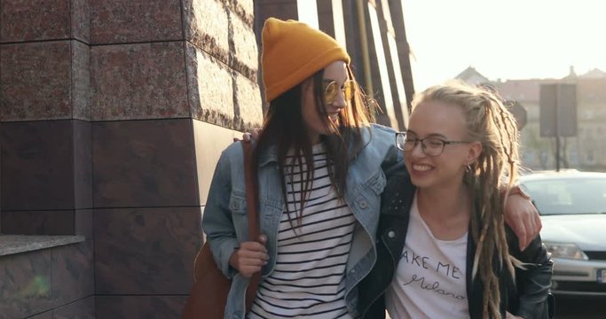 Two Caucasian best female friends in hipster style stepping the city center and emabracing each other while being joyful and happy. Outside.