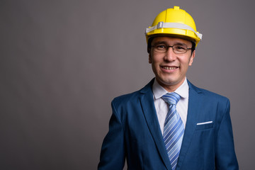 Young Asian businessman wearing hardhat against gray background