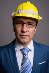 Young Asian businessman wearing hardhat against gray background
