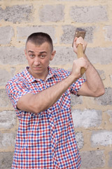 Angry man with sledgehammer on the brick wall background. Working concept