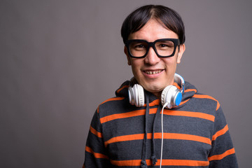 Young Asian nerd man wearing hoodie and headphones against gray 