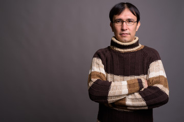 Young Asian nerd man wearing turtleneck sweater against gray bac