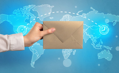 Female hand holding coloured and white envelope with blue map on the background
