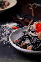 Black pasta spaghetti with seafood and parmesan on a dark style, selective focus.