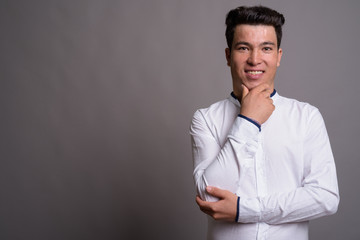Portrait of young Asian businessman against gray background