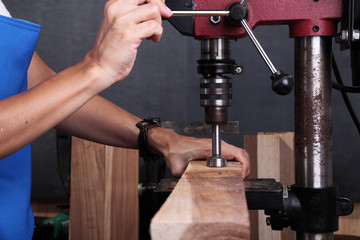 A woman drilling a piece of wood with a bench drill press